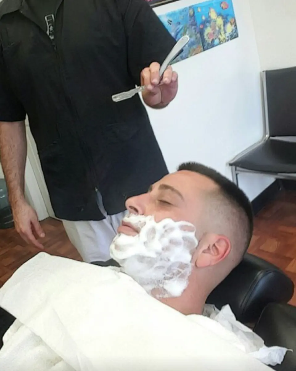 Straight razor shave in progress at Pearl River Barber Shop, client lathered and leaned back in the chair